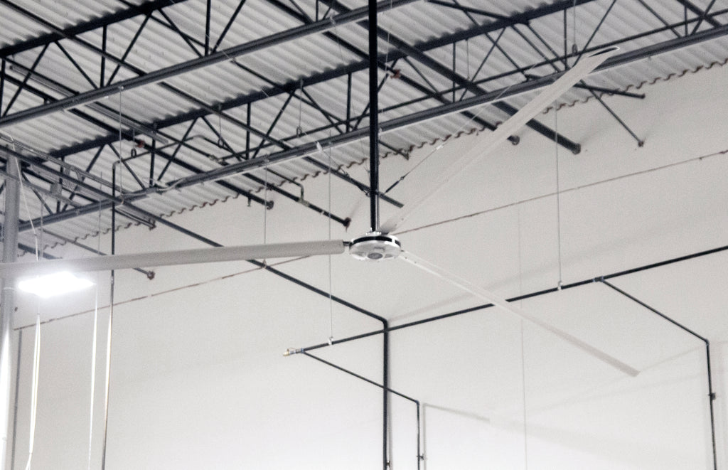 DDI HVLS Industrial Ceiling fan in a warehouse setting with high ceilings and metal beams.