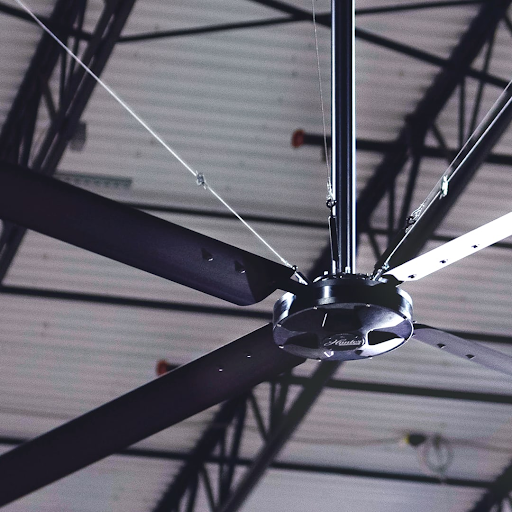 Hunter HVLS ECO ceiling fan mounted to steel truss structure inside a large industrial warehouse facility