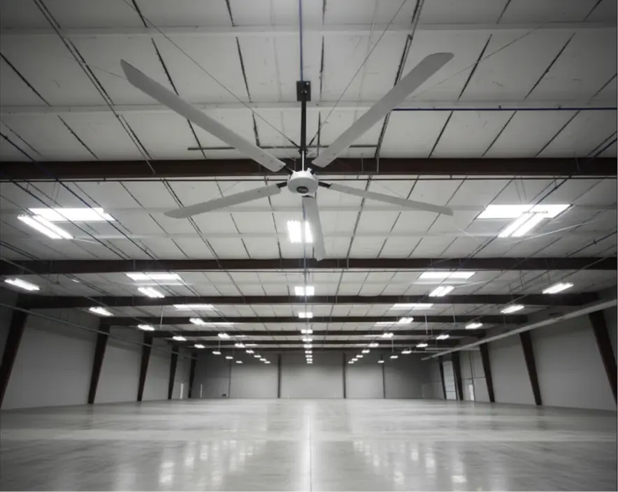 Hunter Titan 20-foot HVLS ceiling fan installed in a large empty warehouse with steel beam ceilings and fluorescent lighting.