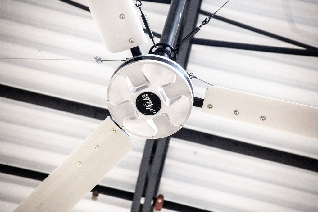 DDI HVLS Industrial Ceiling fan with silver blades and motor installed on a corrugated metal ceiling.